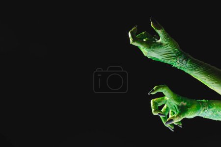 Téléchargez les photos : Mains de monstre vert avec des ongles noirs atteignant sur fond noir. Halloween, concept de tradition et célébration. - en image libre de droit