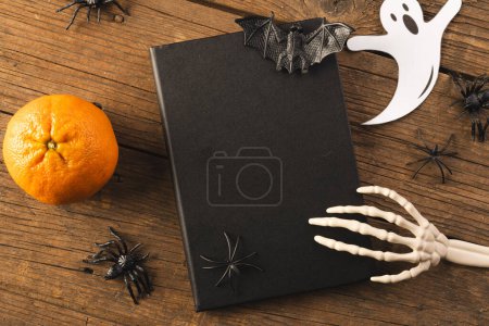 Photo for Halloween decorations and skeleton hand on notebook with copy space on brown background. Fall, autumn, halloween, tradition and celebration concept. - Royalty Free Image