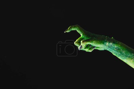 Photo for Green monster hand with black nails pointing with finger on black background. Halloween, tradition and celebration concept. - Royalty Free Image