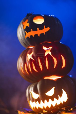 Photo for Vertical image of three illuminating carved pumpkins tower on blue background. Fall, autumn, halloween, tradition and celebration concept. - Royalty Free Image