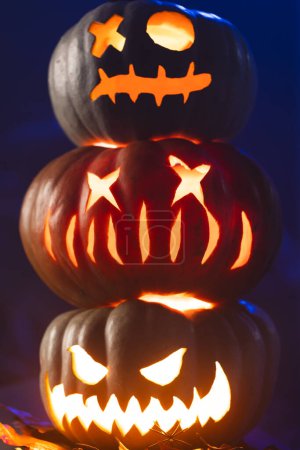 Foto de Imagen vertical de tres calabazas talladas iluminadoras sobre fondo azul. Otoño, otoño, halloween, tradición y concepto de celebración. - Imagen libre de derechos