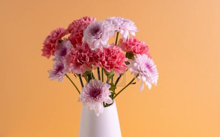 Téléchargez les photos : Fleurs roses dans un vase blanc et copier l'espace sur fond orange. Fleur, plante, forme, nature et concept de couleur. - en image libre de droit