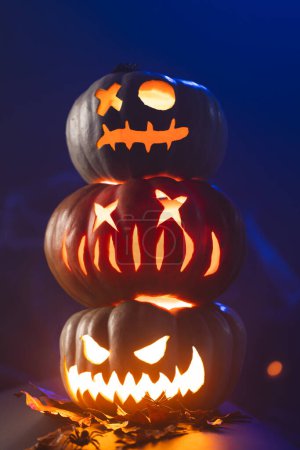 Foto de Imagen vertical de tres calabazas talladas iluminadoras sobre fondo azul. Otoño, otoño, halloween, tradición y concepto de celebración. - Imagen libre de derechos