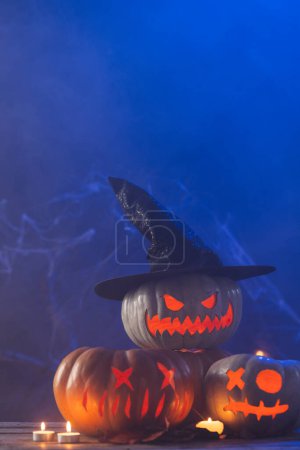Photo for Vertical image of three carved pumpkins and candles with copy space on blue background. Fall, autumn, halloween, tradition and celebration concept. - Royalty Free Image