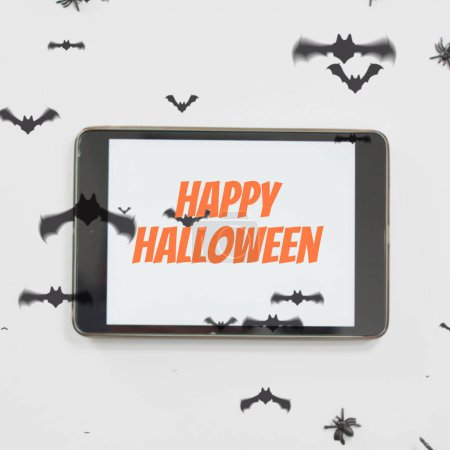 Photo for Composite of happy halloween text on tablet and halloween bats on white background. Halloween, tradition and celebration concept digitally generated image. - Royalty Free Image