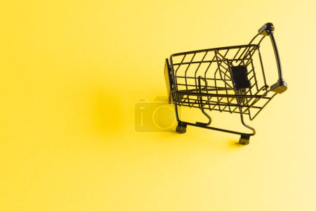 Photo for Black shopping trolley with copy space on yellow background. Cyber shopping, retail, technology, electronic device and communication concept. - Royalty Free Image