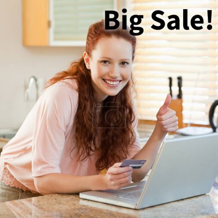 Photo for Big sale text over caucasian woman with thumb up using laptop and credit card in kitchen. Cyber monday, online shopping and sale promotion concept digitally generated image. - Royalty Free Image