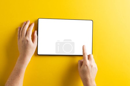 Foto de Manos de mujer caucásica usando tableta con pantalla en blanco y espacio de copia sobre fondo amarillo. Tecnología cibernética, dispositivo electrónico y concepto de comunicación. - Imagen libre de derechos