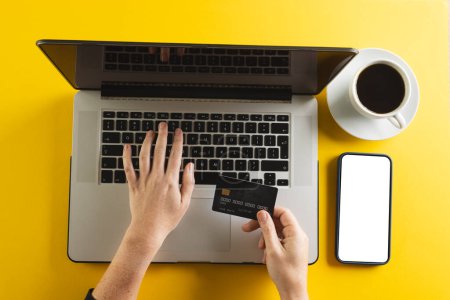Photo for Caucasian woman with credit card using laptop and smartphone with copy space on yellow background. Cyber shopping, retail, technology, electronic device and communication concept. - Royalty Free Image