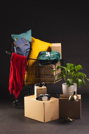 Photo for Vertical image of shopping trolley with shopping, boxes, plant and copy space over black background. Cyber monday, black friday, online shopping, shipping and global connections concept. - Royalty Free Image