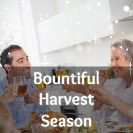 Photo for Bountiful harvest season text over happy caucasian family toasting at thanksgiving dinner. Thanksgiving, harvest festival, american tradition, family and autumn celebration digitally generated image. - Royalty Free Image