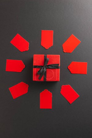 Foto de Imagen vertical de etiquetas de regalo rojas en círculo y caja de regalo roja con espacio de copia sobre fondo negro. Cyber lunes, viernes negro, compras en línea, envío y concepto de conexiones globales. - Imagen libre de derechos