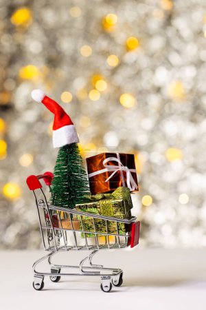 Photo for Vertical image of shopping trolley with gifts and christmas fairy lights with copy space background. Christmas, decorations, tradition and celebration concept. - Royalty Free Image