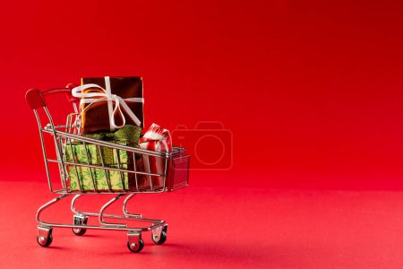 Téléchargez les photos : Chariot d'achat avec cadeaux de Noël avec espace de copie sur fond rouge. Noel, décoration, tradition et concept de célébration. - en image libre de droit