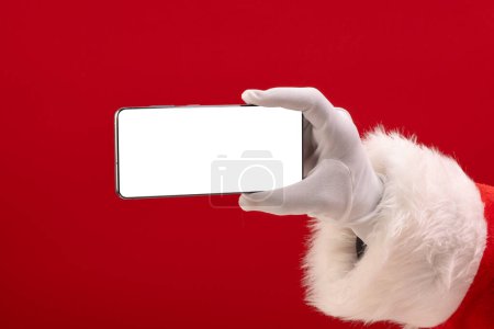 Photo for Santa claus holding smattphone with copy space on red background. Santa claus, technology, christmas, tradition and celebration concept. - Royalty Free Image