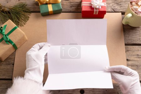 Photo for Santa claus holding letter with copy space and christmas presents on wooden background. Santa claus, christmas, tradition and celebration concept. - Royalty Free Image