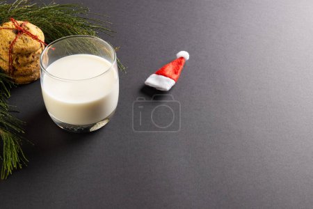 Foto de Vaso de leche, galletas de Navidad y sombrero de Santa Claus con espacio para copias en fondo negro. Dulces, Navidad, tradición y concepto de celebración. - Imagen libre de derechos