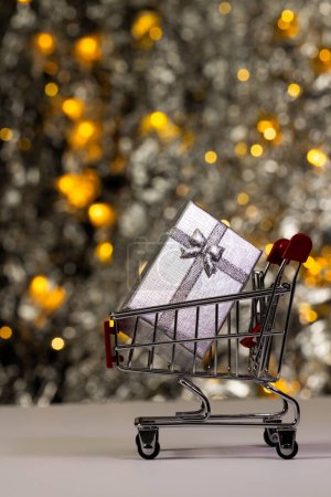 Photo for Vertical image of shopping trolley with gift and christmas tree with copy space background. Christmas, decorations, tradition and celebration concept. - Royalty Free Image