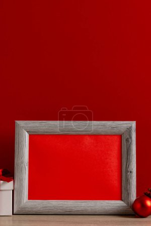 Foto de Imagen vertical de decoraciones de chrsitmas y marco de madera con espacio de copia sobre fondo rojo. Navidad, decoraciones, tradición y concepto de celebración. - Imagen libre de derechos