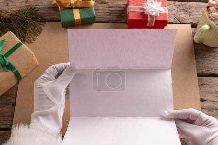 Téléchargez les photos : Santa Claude tenant lettre avec espace de copie et cadeaux de Noël sur fond en bois. Père Noël, Noël, concept de tradition et de célébration. - en image libre de droit