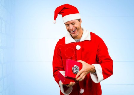 Foto de Hombre caucásico con traje de santa apertura regalo de Navidad contra el espacio de copia sobre fondo azul. concepto de navidad y festividad - Imagen libre de derechos