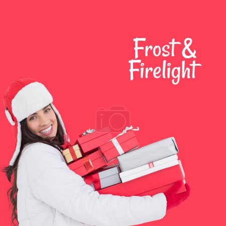 Photo for Frost and firelight text on red with happy caucasian woman holding christmas gifts. Celebration of winter, seasonal greeting and christmas traditions, digitally generated image. - Royalty Free Image