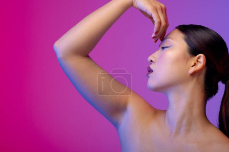 Foto de Mujer asiática con delineador de ojos azul y esmalte de uñas rojo sobre fondo púrpura. Cosméticos, maquillaje, moda femenina y belleza, inalterados. - Imagen libre de derechos