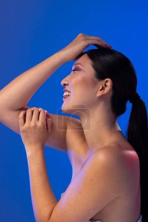 Foto de Mujer asiática con cabello negro con sombra de ojos púrpura y esmalte de uñas rojo sobre fondo azul. Cosméticos, maquillaje, moda femenina y belleza, inalterados. - Imagen libre de derechos