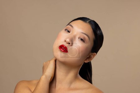 Foto de Retrato de mujer asiática con lápiz labial rojo y esmalte de uñas sobre fondo beige. Cosméticos, maquillaje, moda femenina y belleza, inalterados. - Imagen libre de derechos