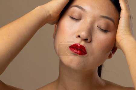 Téléchargez les photos : Femme asiatique portant rouge à lèvres et vernis à ongles sur fond beige. Cosmétiques, maquillage, mode féminine et beauté, inchangés. - en image libre de droit