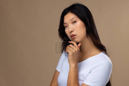 Téléchargez les photos : Portrait de femme asiatique portant un maquillage naturel et un t-shirt blanc sur fond beige, espace de copie. Cosmétiques, maquillage, mode féminine et beauté, inchangés. - en image libre de droit