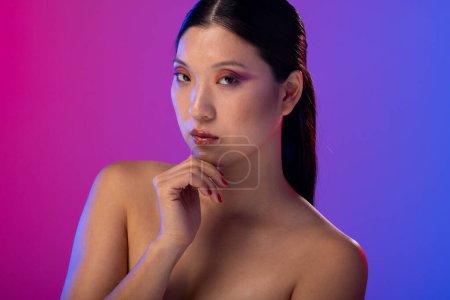 Foto de Retrato de mujer asiática con sombra de ojos morada y esmalte de uñas rojo sobre fondo morado. Cosméticos, maquillaje, moda femenina y belleza, inalterados. - Imagen libre de derechos