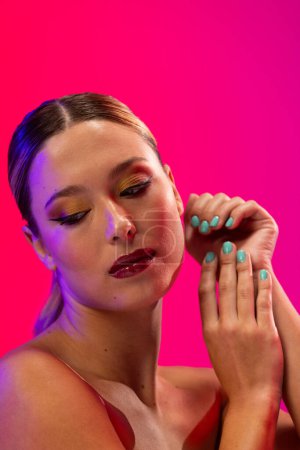 Foto de Mujer caucásica con lápiz labial rojo y esmalte de uñas azul sobre fondo rosa. Cosméticos, maquillaje, moda femenina y belleza, inalterados. - Imagen libre de derechos