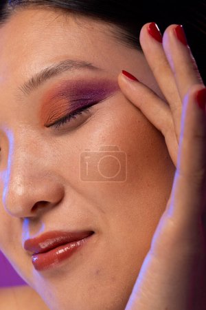 Photo for Close up of asian woman wearing purple eye shadow and red nail polish on purple background. Cosmetics, makeup, female fashion and beauty, unaltered. - Royalty Free Image