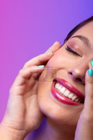 Foto de Mujer caucásica con lápiz labial rosa y esmalte de uñas azul sobre fondo púrpura, espacio para copiar. Cosméticos, maquillaje, moda femenina y belleza, inalterados. - Imagen libre de derechos