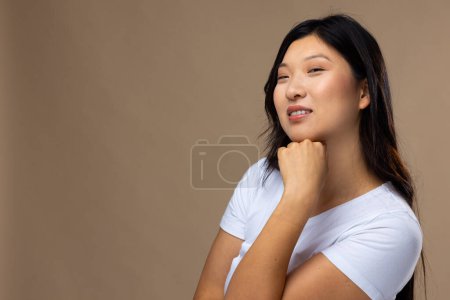 Téléchargez les photos : Portrait de femme asiatique portant un maquillage naturel et un t-shirt blanc sur fond beige, espace de copie. Cosmétiques, maquillage, mode féminine et beauté, inchangés. - en image libre de droit