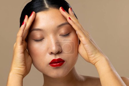 Foto de Mujer asiática con lápiz labial rojo y esmalte de uñas sobre fondo beige. Cosméticos, maquillaje, moda femenina y belleza, inalterados. - Imagen libre de derechos
