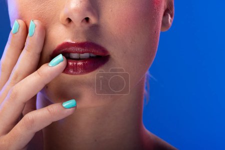 Photo for Caucasian woman wearing red lipstick and blue nail polish on blue background. Cosmetics, makeup, female fashion and beauty, unaltered. - Royalty Free Image