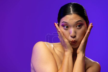 Photo for Asian woman with black hair wearing purple eye shadow and red nail polish on purple background. Cosmetics, makeup, female fashion and beauty, unaltered. - Royalty Free Image