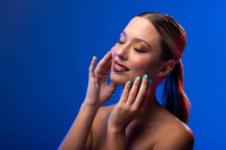 Foto de Mujer caucásica con lápiz labial rojo y esmalte de uñas azul sobre fondo azul, espacio para copiar. Cosméticos, maquillaje, moda femenina y belleza, inalterados. - Imagen libre de derechos