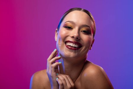 Foto de Retrato de mujer caucásica con lápiz labial rojo y esmalte de uñas azul sobre fondo púrpura. Cosméticos, maquillaje, moda femenina y belleza, inalterados. - Imagen libre de derechos