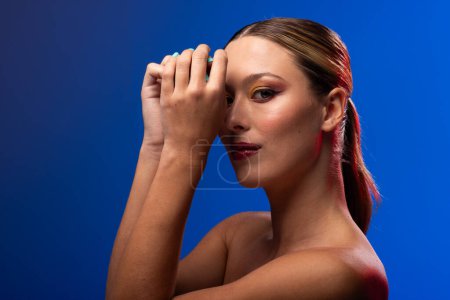 Photo for Portrait of caucasian woman wearing golden eye shadow and blue nail polish on blue background. Cosmetics, makeup, female fashion and beauty, unaltered. - Royalty Free Image