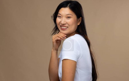 Photo for Portrait of asian woman wearing natural makeup and white t-shirt on beige background, copy space. Cosmetics, makeup, female fashion and beauty, unaltered. - Royalty Free Image