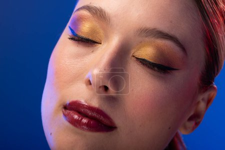 Photo for Caucasian woman with brown hair wearing golden eye shadow and red lipstick on blue background. Cosmetics, makeup, female fashion and beauty, unaltered. - Royalty Free Image