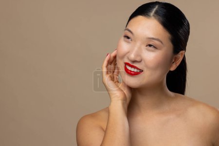 Téléchargez les photos : Femme asiatique portant rouge à lèvres et vernis à ongles sur fond beige, espace de copie. Cosmétiques, maquillage, mode féminine et beauté, inchangés. - en image libre de droit