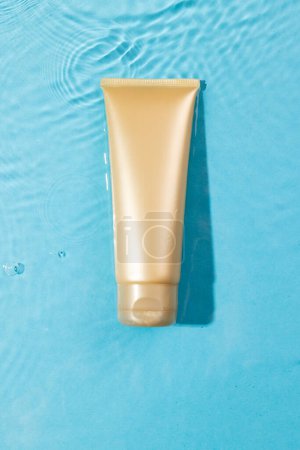 Photo for Vertical image of beauty product tube in water with copy space background on blue background. Health and beauty, make up and beauty concept. - Royalty Free Image