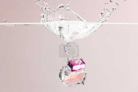 Téléchargez les photos : Produit de beauté bouteille de parfum tombant dans l'eau avec l'espace de copie arrière-plan sur fond rose. Santé et beauté, concept maquillage et beauté. - en image libre de droit