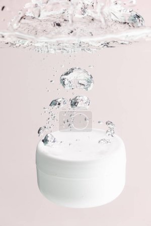 Photo for Vertical image of beauty product tub falling into water, copy space background on pink background. Health and beauty, make up and beauty concept. - Royalty Free Image