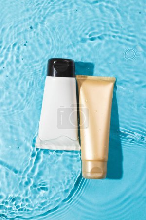 Photo for Vertical image of beauty product tubes in water with copy space background on blue background. Health and beauty, make up and beauty concept. - Royalty Free Image