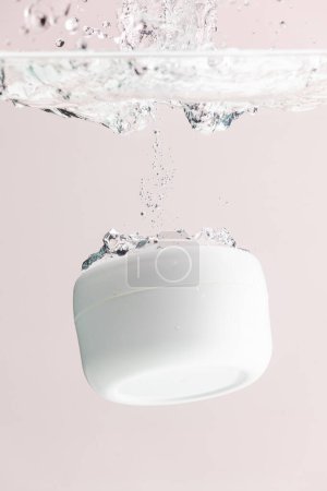 Téléchargez les photos : Image verticale de la baignoire de produit de beauté tombant dans l'eau, copiez le fond de l'espace sur fond rose. Santé et beauté, concept maquillage et beauté. - en image libre de droit